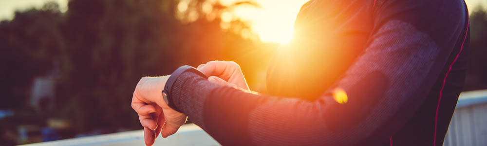 Close-up of woman's torso, she has one hand on her smart watch. Sun is bright in the background. Close-up of woman's torso, she has one hand on her smart watch. Sun is bright in the background.
